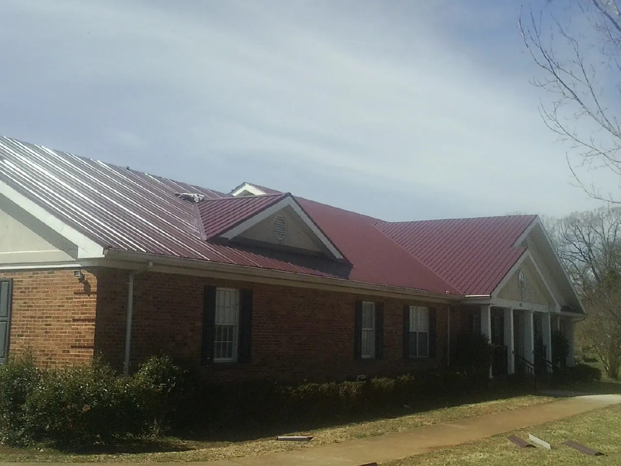 Red metal roof with gabled entries on a long brick building, from a Hail Damage Roof Repair job in Airville