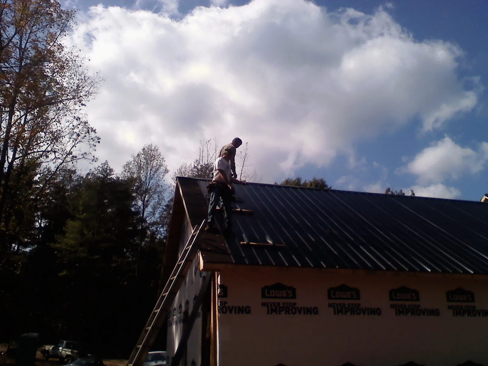 Roofer fastening dark metal panels high against a cloudy sky, from a Roof Inspection job in Airville