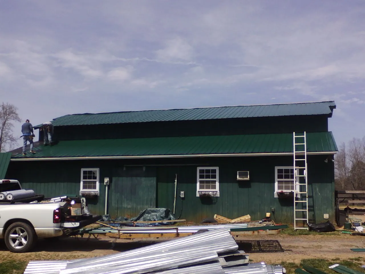 Crew installing green metal roofing on a large green barn in Airville