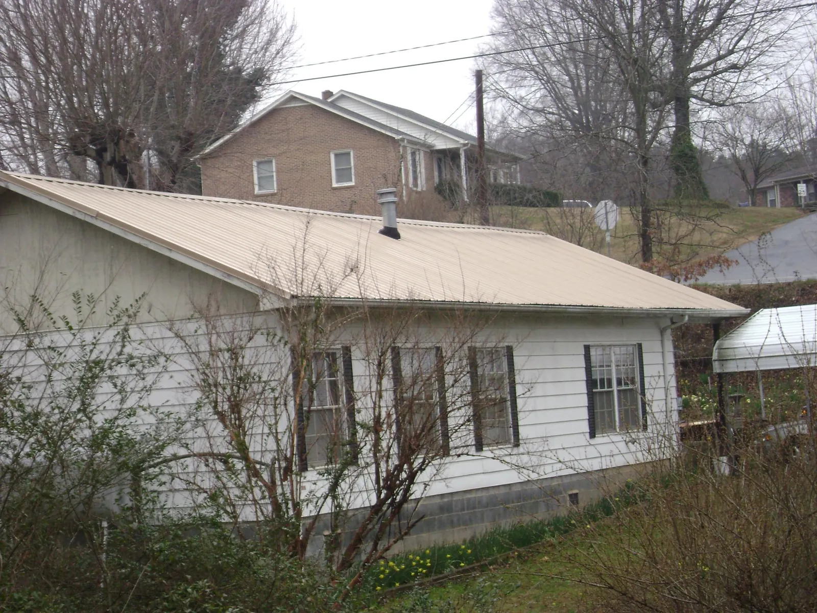 Tan metal roof on a white sided house set into a hillside — Commercial Roofing by Roofing Brothers in Airville